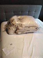 Photo of the queen size comforter and pillow shams packed in plastic on a mattress with a quilted pattern.