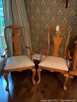 Photo showing two Thomasville pecan wood captain chairs with upholstered seats against patterned wallpaper and curtain, highlighting wood finish and chair shape.