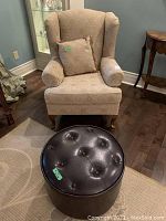 Wingback chair and ottoman taken from frontal angle showing upholstery, pillow, wooden legs, no visible fabric damage but minor scratches on chair legs.