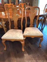 Front view of two dining chairs showing pecan wood finish and cream-gold floral upholstered seats.