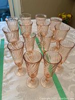 Group photo of fourteen pink glasses arranged on table: six champagne flutes and eight wine glasses, showing overall style and color