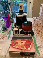 Tassimo Bosch coffee maker, Epicure stainless steel milk frother, red electric fondue pot on black base, boxed 4-piece black fondue plate set arranged on table