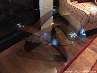 Full view of the glass top coffee table showing the oval clear glass surface and curved dark wood base with metal disc supports.