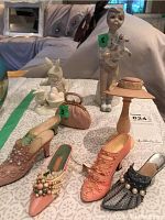 Photo showing porcelain figurine of boy with bird, child in animal costume, decorative shoes and small pink purse on patterned surface.