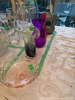 Five pieces of coloured glass including pink candy dish in front, purple and red-purple vases behind, and multicoloured vase