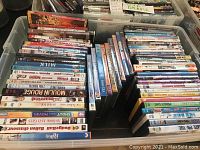 Top-down photo showing numerous DVD cases stacked inside a large plastic storage bin, titles visible on the spines such as Dodge Ball, Moulin Rouge, Ice Age, and more.