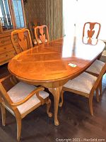 Oval pecan wood dining table with cabriole legs and part of dining chairs around it, showing the full table shape and finish.