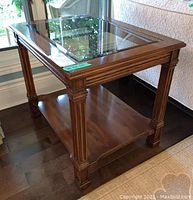 Side view of one end table showing the wooden legs with carved detailing and the smoked glass framed top surface.