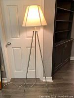 Full view of the floor lamp showing brushed nickel tripod legs, white canvas-look shade, and silver translucent cord.