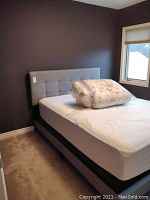 Full view of bed with fabric covered headboard and mattress on frame, two pillows on mattress