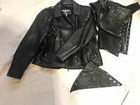 Black genuine leather ladies motorcycle jacket with matching chaps laid out flat showing front view and details.
