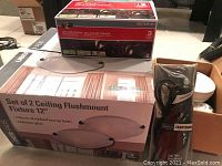 Boxed set of 2 UberHaus ceiling flush mount light fixtures 12 inch, Sephora finish, alabaster glass, Sears Craftsman electric engraver in plastic packaging, and Hampton Bay LED low voltage spotlight kit boxed.