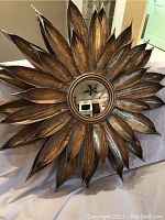 Full front view showing gold-toned metal sunburst design and center round mirror reflecting interior ceiling fan and lights.