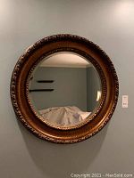 Full view of the round mirror hanging on a wall showing its size and oval carvings in the frame