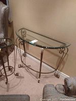 Full view of demilune table showing clear glass top and wrought iron base near wall.