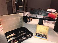 Craftsman router table on display with two plastic cases containing various router bits, bits appear assorted including ones with red handles and metal shaft bits.