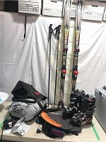 Full view of Rossignol skis with Salomon bindings, poles, ski boots, boot bag, and air mattress package on floor.