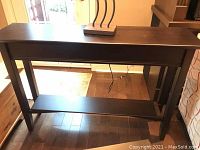 Full view of the wooden sofa table with tapered legs and lower shelf in dark finish.