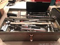 Metal toolbox open showing assortment of hand tools including sockets, ratchets, extensions.