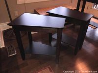 Two dark wood tapered end tables with lower shelves together in a room.