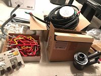 Photo showing box with multiple vinyl coated wall hooks (red and yellow) with screw ends, Dyson motor part components, and coiled A/V cables.