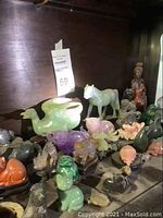 Shelf view showing white jade horse, green jade duck, various small stone animals and seated figure.