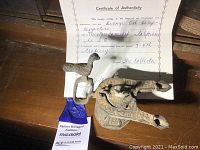 Oil lamp displayed with certificate of authenticity visible behind it on wooden surface.