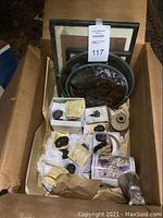 Overall cardboard box contents showing sculptures, framed print, vase, tin and stained glass