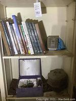 Shelf containing various hardcover books and decorative boxes, showing dust accumulation