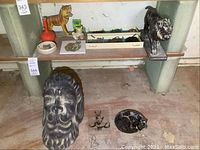 Overview of shelf and floor showing all items: carved tiger, glass bottle, saucer, cat head figurine, storage box on shelf; lion head sculpture, wire puzzle, glass panel, cat ashtray, metal lion figure on floor