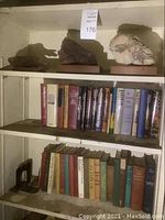 Shelf with three decorative stone sculptures on wooden bases and two shelves of hardcover books.