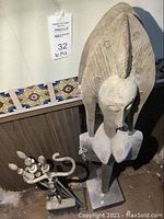 Main shot showing large carved wood tribal figure leaning against wall next to 6-piece metal fireplace tool set on stand; dusty surfaces.