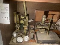 Two brass microscopes, dial gauges and optical instrument parts on shelf