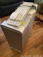 Apple Mac Pro tower computer in silver aluminum with one power cord connected and two white Apple keyboards and two white Apple mice placed on top, cables draped over the case.