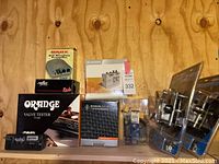 Shelf display of Nady Audio DMP-2 preamp box, Reflex Pickups box, Orange VT-1000 valve tester box, Warwick tuner, M-Audio CO2 interface box