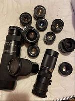 Full assortment of camera lenses arranged on a surface showing different sizes and types including large telephoto and smaller lenses.