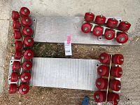 Overview of both aluminum plates each with 14 red skateboard wheels laid on ground
