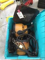 Two orange cylindrical Ianaro film lights with barn doors and attached cables stored in a teal plastic bin.