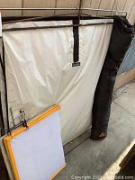 Photo of large metal frame diffusion panels with white fabric and smaller square frames with yellow borders leaning against wall with black carrying case