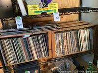 Two wooden crates on metal shelving filled with upright vinyl records and a few loose sleeves on top.