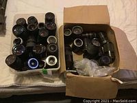Two containers (plastic bin and cardboard box) filled with assorted manual focus camera lenses