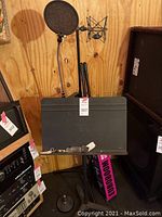 Microphone stand with pop filter, shock mount, and music stand with attached clip positioned together against a wooden wall.