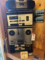 Overview showing entire stack: Aiwa boombox atop Tandberg TCD 310 MkII cassette deck, TEAC A-3340S reel-to-reel recorder below, two Matchbox Pro patch boxes mounted to wall right, Electro-Voice mic on bench