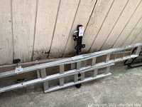 Full view of the aluminum cargo carrier laid flat against a wall showing the foldable side rails and base grid platform.