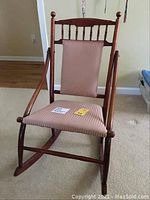 Front view showing wooden spindle backrest, upholstered seat with pink striped fabric, and curved rockers on the bottom.