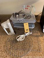 Overview of the lot showing the hand mixer, two baking pans with lids, Pyrex measuring cup, and cooling racks on kitchen counter.
