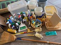 Wide view of cleaning chemicals, brooms, mop, buckets, dish drainer and cutting board showing full assortment of items.