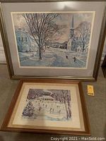 Two framed prints displayed together showing winter landscapes with snow-covered streets and houses with clear signatures.