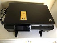 HP Photosmart 5510 printer showing front panel with touchscreen, paper output tray with paper inside, power cord connected, and top closed.