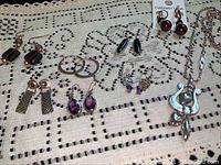 Assorted costume jewelry including six pairs of earrings and one necklace laid out on a crocheted lace tablecloth.